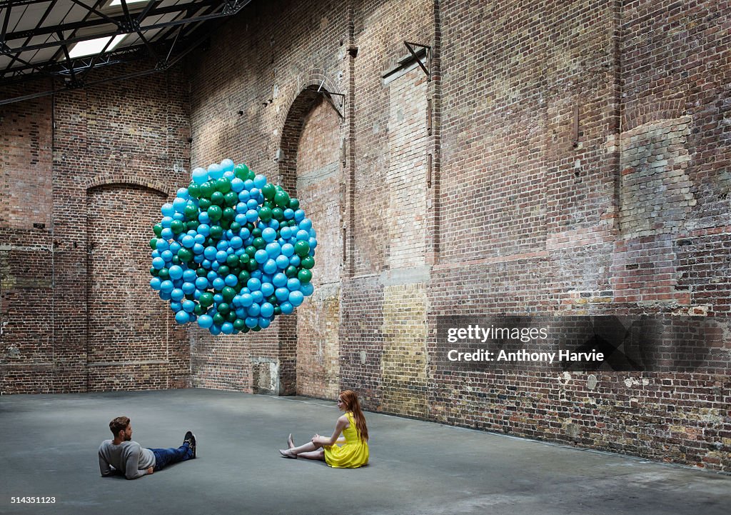 Couple in warehouse with globe made of balloons