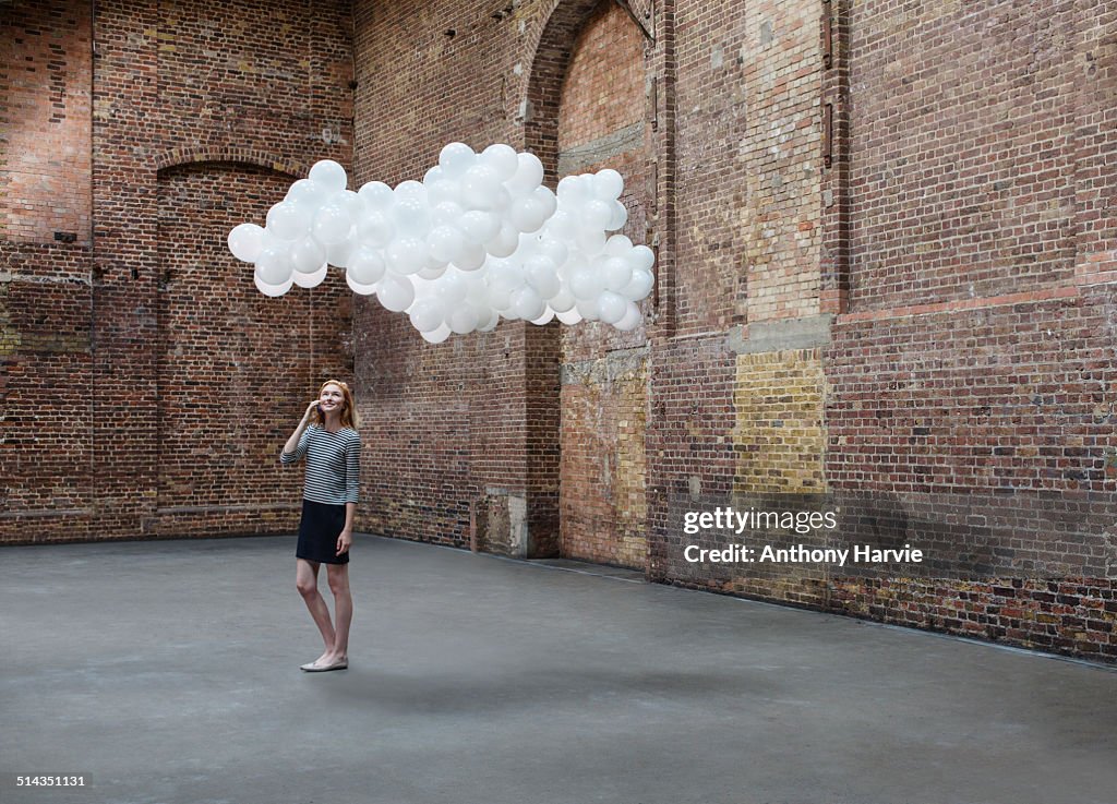 Woman in warehouse, cloud of balloons above head