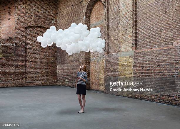 woman in warehouse, cloud of balloons above head - cloud computing stock-fotos und bilder