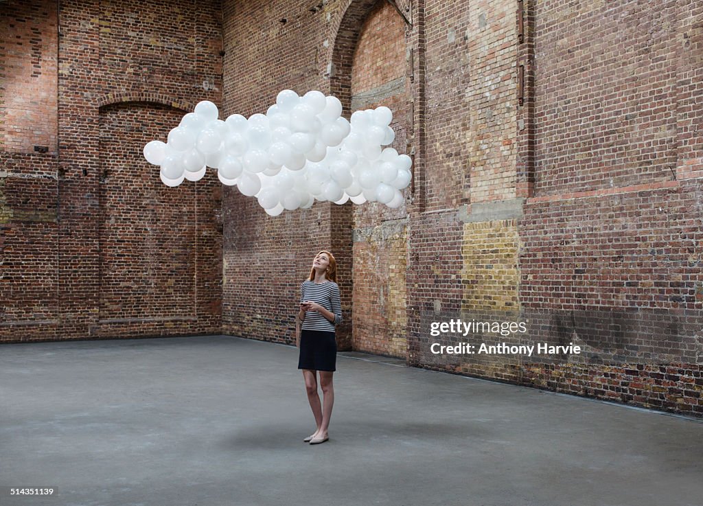 Woman in warehouse, cloud of balloons above head