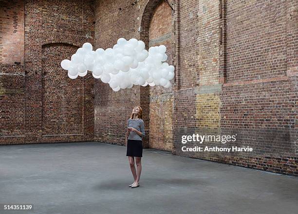 woman in warehouse, cloud of balloons above head - balloons concept imagens e fotografias de stock