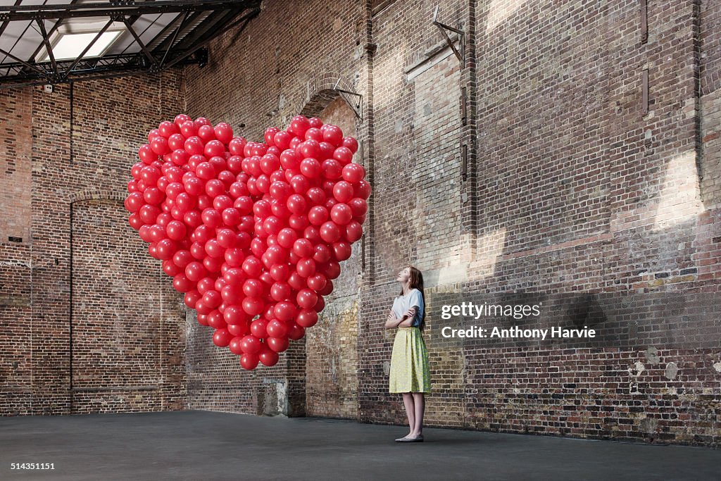 Woman in warehouse with heart made of balloons