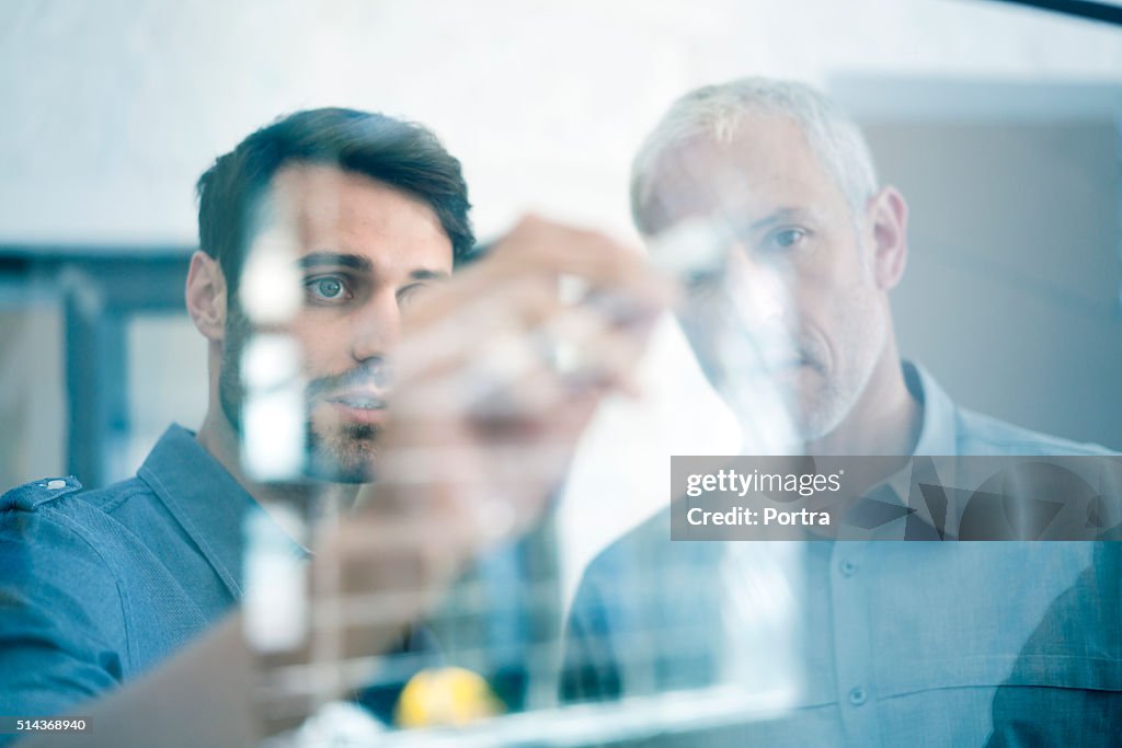 Hombres de negocios haciendo un Plan de en la pared de vidrio en oficina