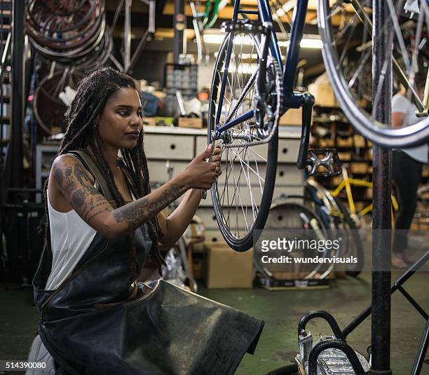 frau mit dem fahrrad mechaniker reparieren eine steuer in einer werkstatt reparieren - african american mechanic stock-fotos und bilder