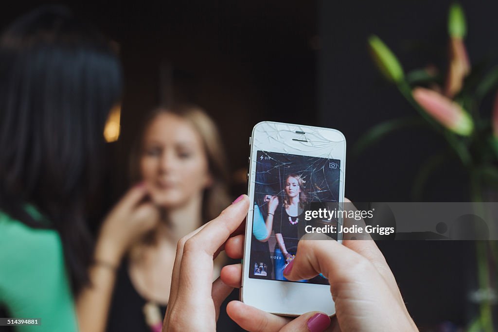 Woman taking photo of friend getting make-up done