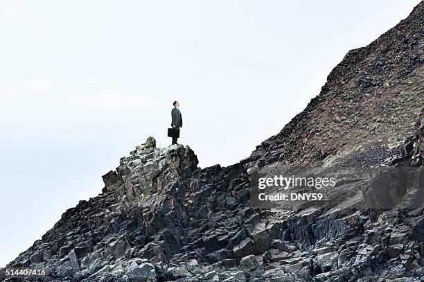 businessman on a rocky slope looks at the challenges ahead - businessman challenge stock pictures, royalty-free photos & images