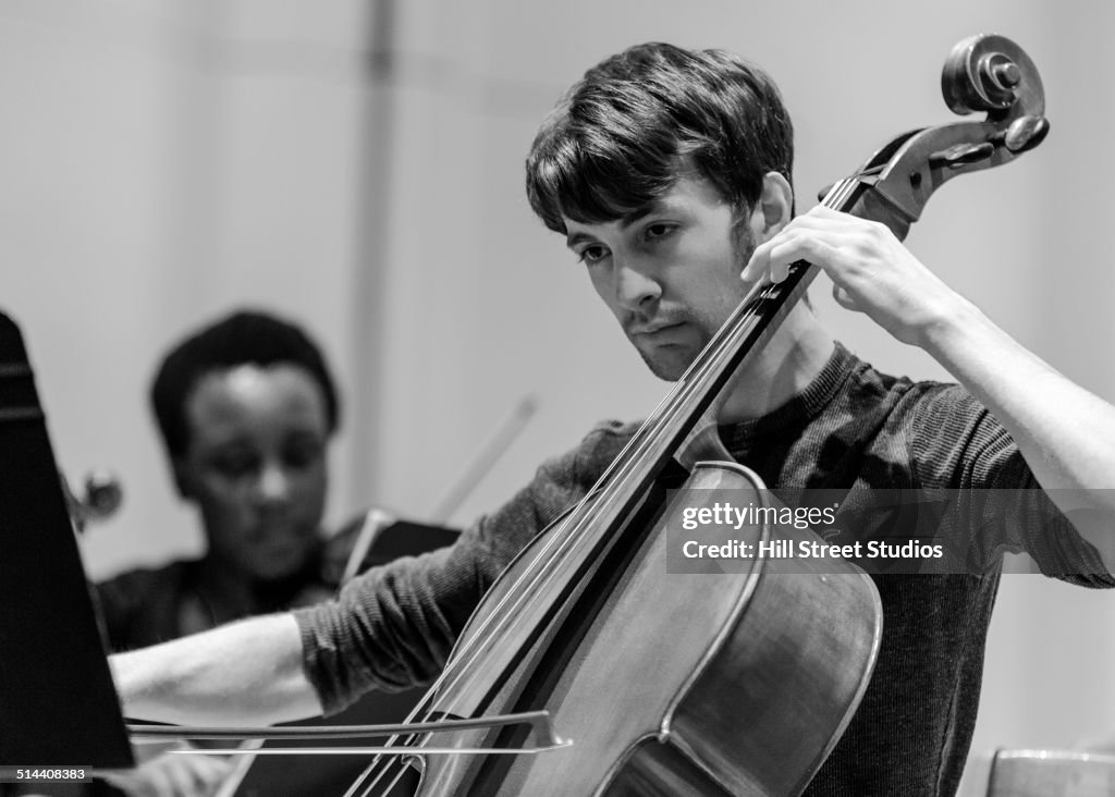 Caucasian student playing cello in college orchestra