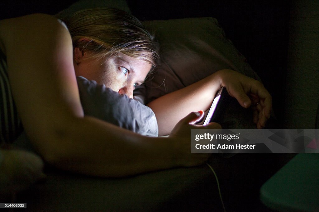 Caucasian woman using cell phone in bed