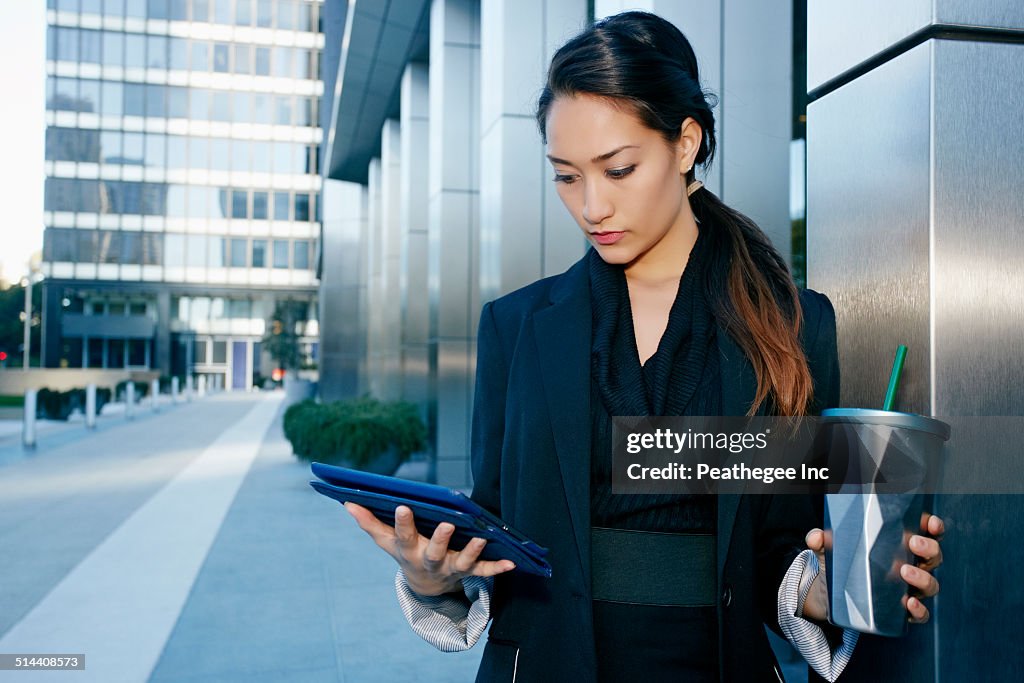 Mixed race businesswoman using tablet computer on city street