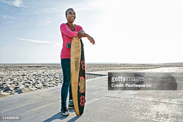 older black woman holding skateboard on beach - woman african sport stockfoto's en -beelden