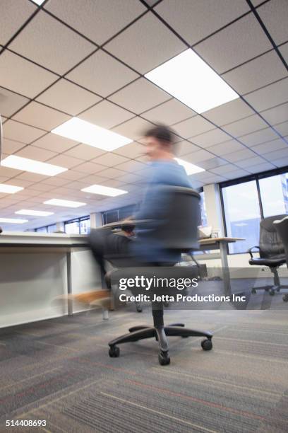 blurred view of caucasian businessman spinning in office chair - bürostuhl stock-fotos und bilder