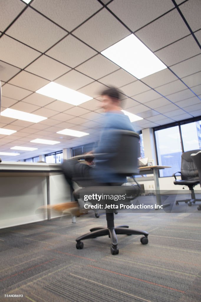 Blurred view of Caucasian businessman spinning in office chair