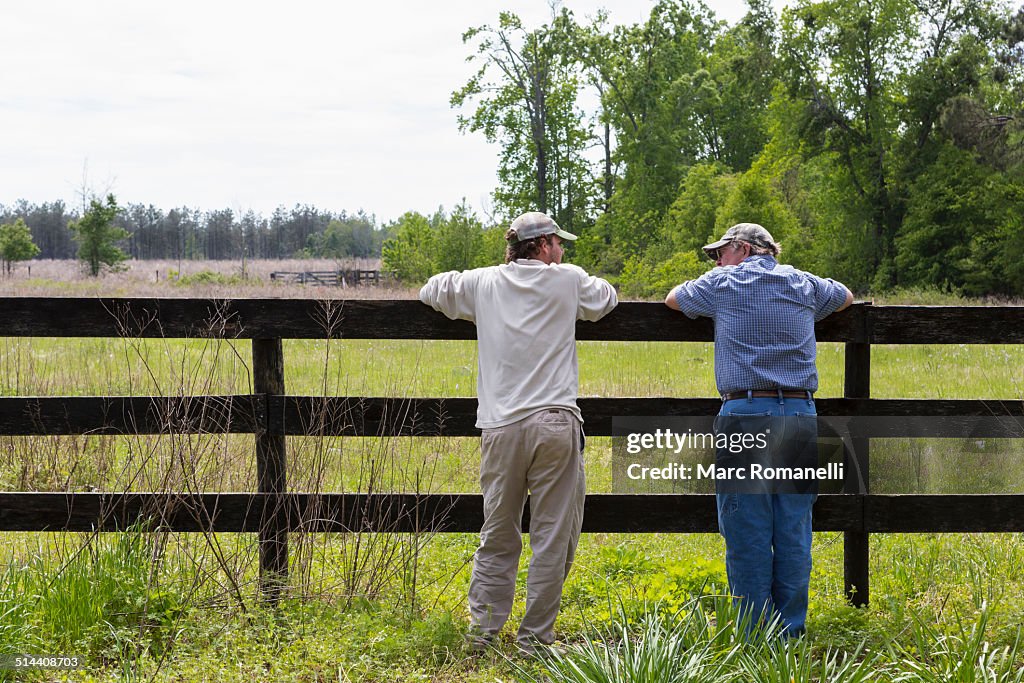 Caucasian father and son leaning on fence by rural field