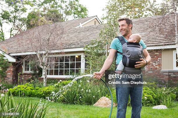 caucasian father holding baby and watering plants - portabebés fotografías e imágenes de stock