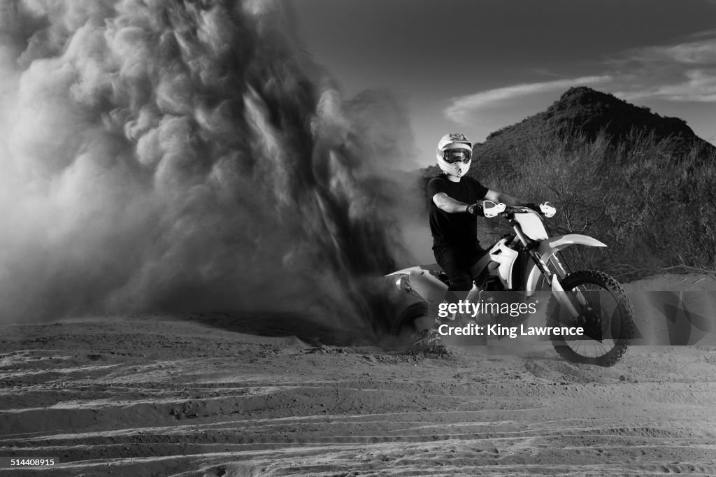 Caucasian man riding dirt bike in dust cloud