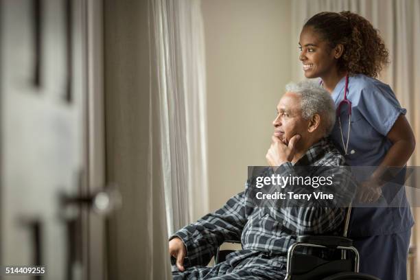 african american nurse wheeling senior patient - holistic patient care stock-fotos und bilder