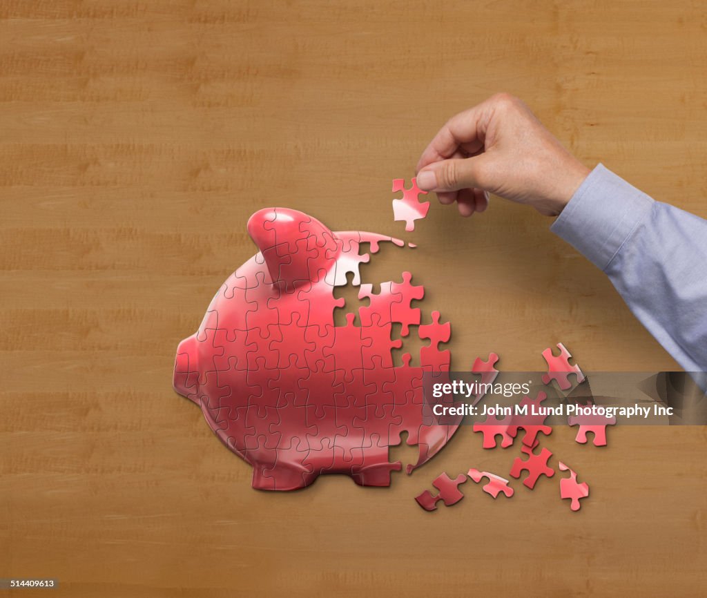 Businessman putting together piggy bank puzzle on desk