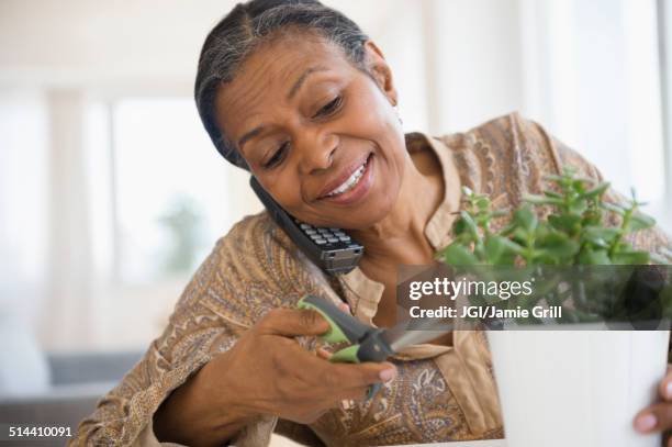 mixed race woman trimming plant and talking on phone - festnetzanschluss stock-fotos und bilder