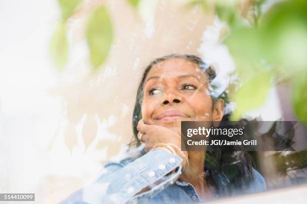 mixed race woman looking out window - um dia na vida de imagens e fotografias de stock