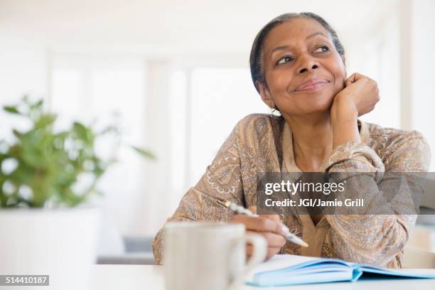 mixed race woman writing at desk - diary stockfoto's en -beelden