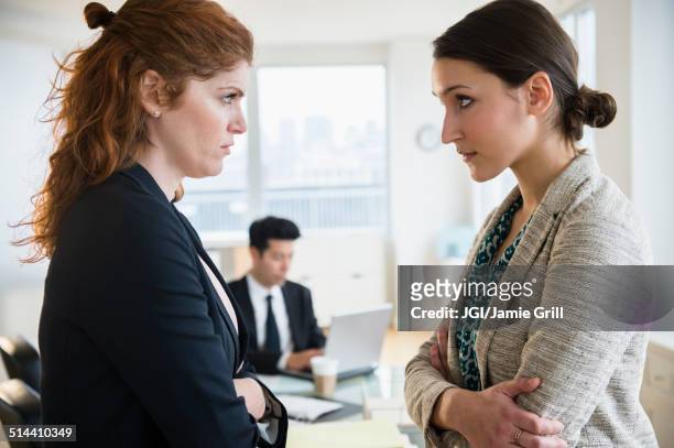 businesswomen glaring at each other in office - rivaliteit stockfoto's en -beelden