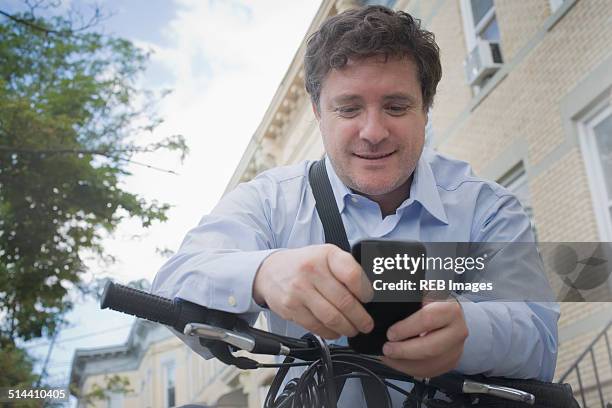 hispanic businessman using cell phone on bicycle on city street - chilean ethnicity stock pictures, royalty-free photos & images