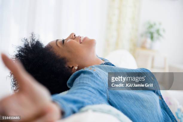 african american woman with arms outstretched on sofa - human limb stock pictures, royalty-free photos & images