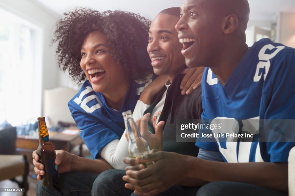 Friends drinking beer and cheering at game on television