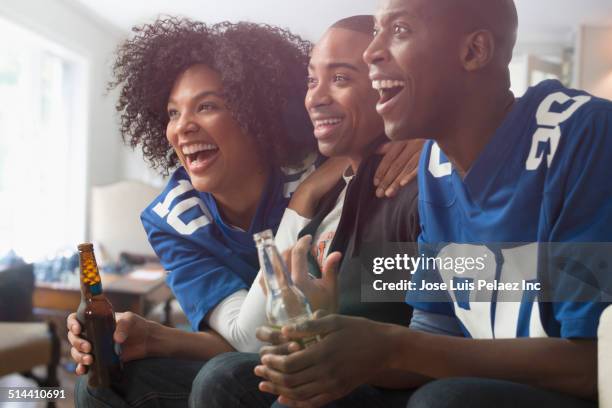 friends drinking beer and cheering at game on television - woman in sports jersey stock pictures, royalty-free photos & images