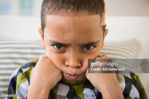 mixed race boy pouting on sofa - tegendraads stockfoto's en -beelden