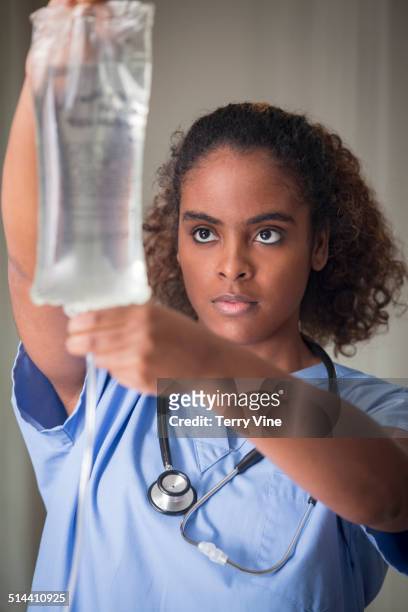 african american nurse holding adjusting iv bag in hospital - hemodialisis fotografías e imágenes de stock