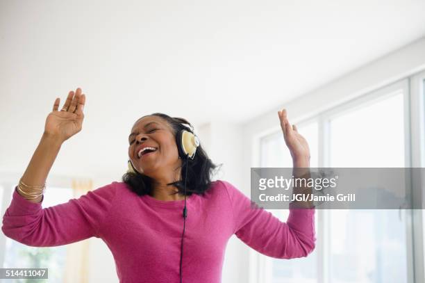 mixed race woman listening to headphones in living room - rhythm stockfoto's en -beelden