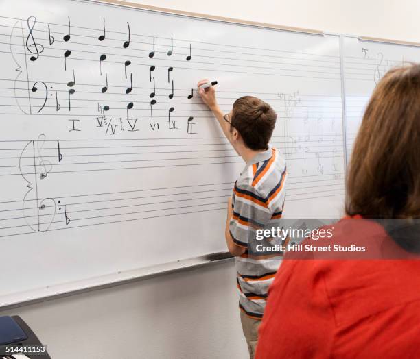 caucasian student writing on board in music class - two female teachers blackboard stockfoto's en -beelden