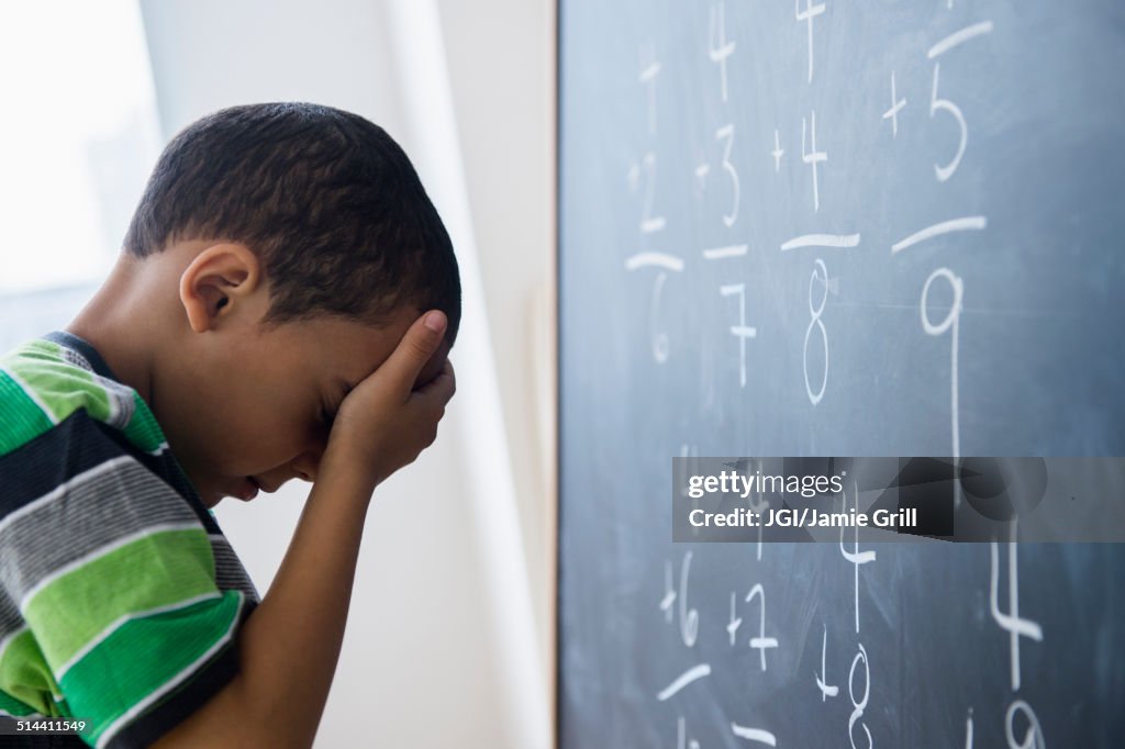 Mixed race boy doing math problems at board in class