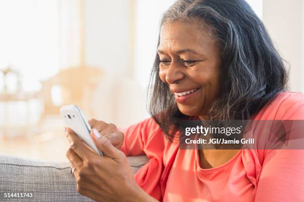 mixed race woman using cell phone on sofa - african lady sitting and looking at her smartphone stock-fotos und bilder