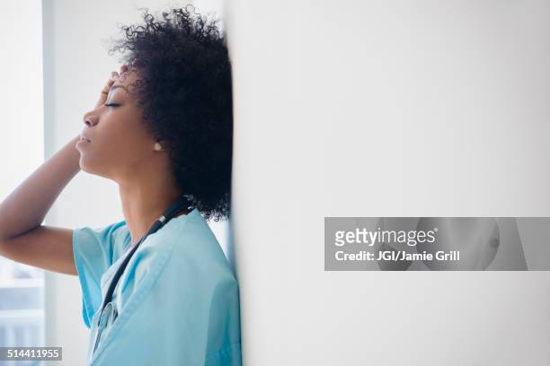 african american nurse leaning against wall - arzt profil stock-fotos und bilder