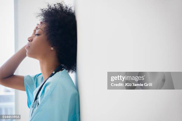 african american nurse leaning against wall - sad nurse stock pictures, royalty-free photos & images