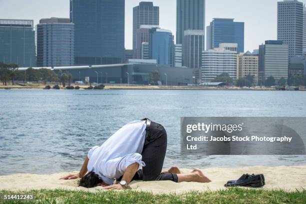 hispanic businessman burying his head in sand on beach, perth, western australia, australia - burying stockfoto's en -beelden