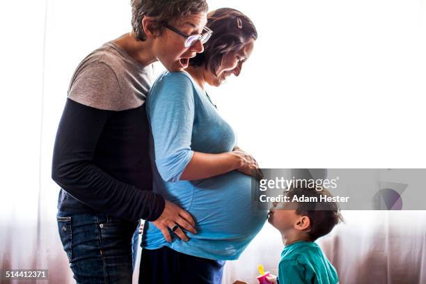 lesbian couple with son standing by window - lesbische stock-fotos und bilder