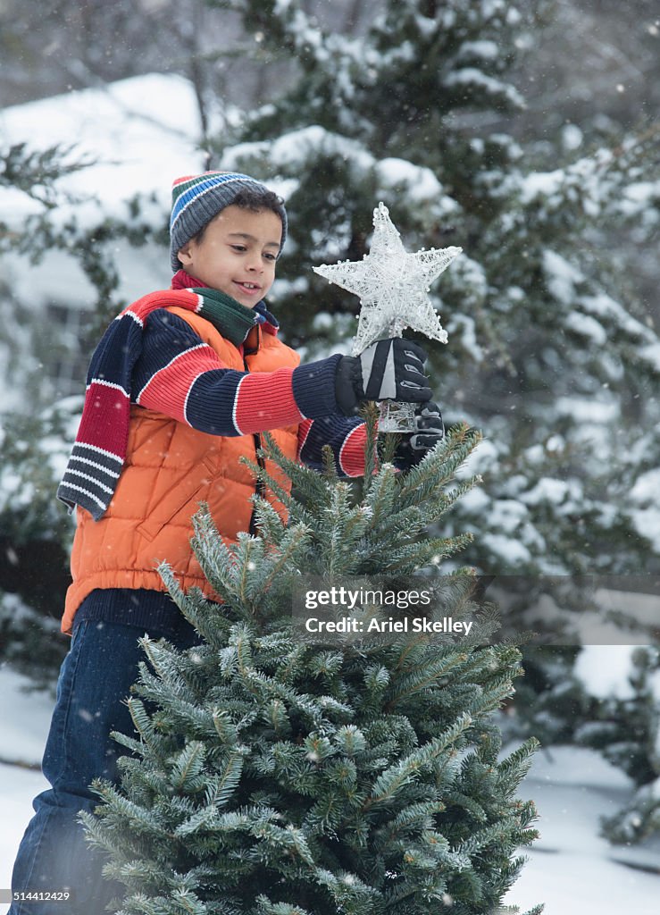 Boy decorating Christmas tree in snow outdoors