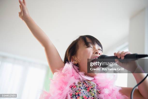 filipino girl singing karaoke in living room - child singing stock-fotos und bilder