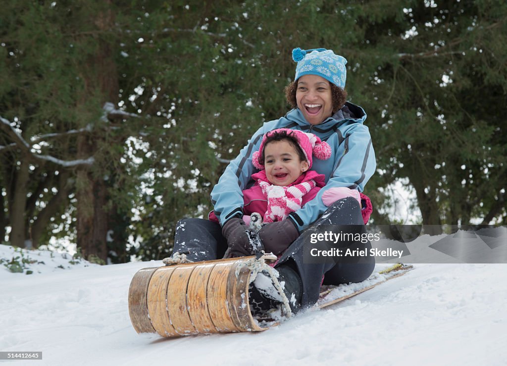 Mother and daughter sledding on snowy hill outdoors