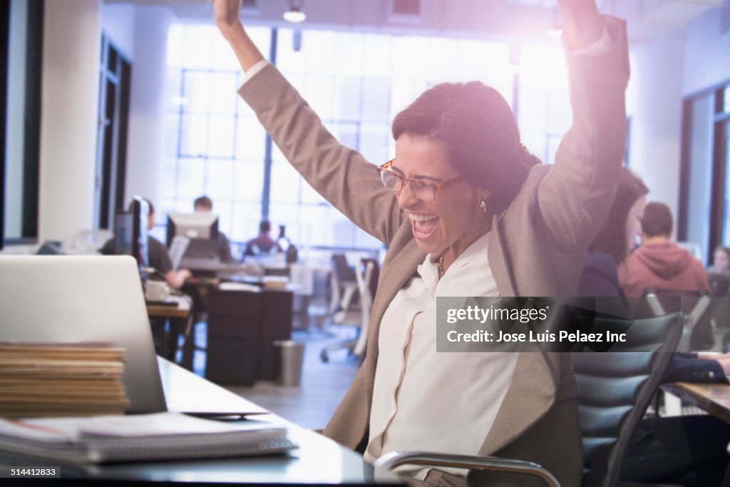 Hispanic businesswoman cheering at laptop in office