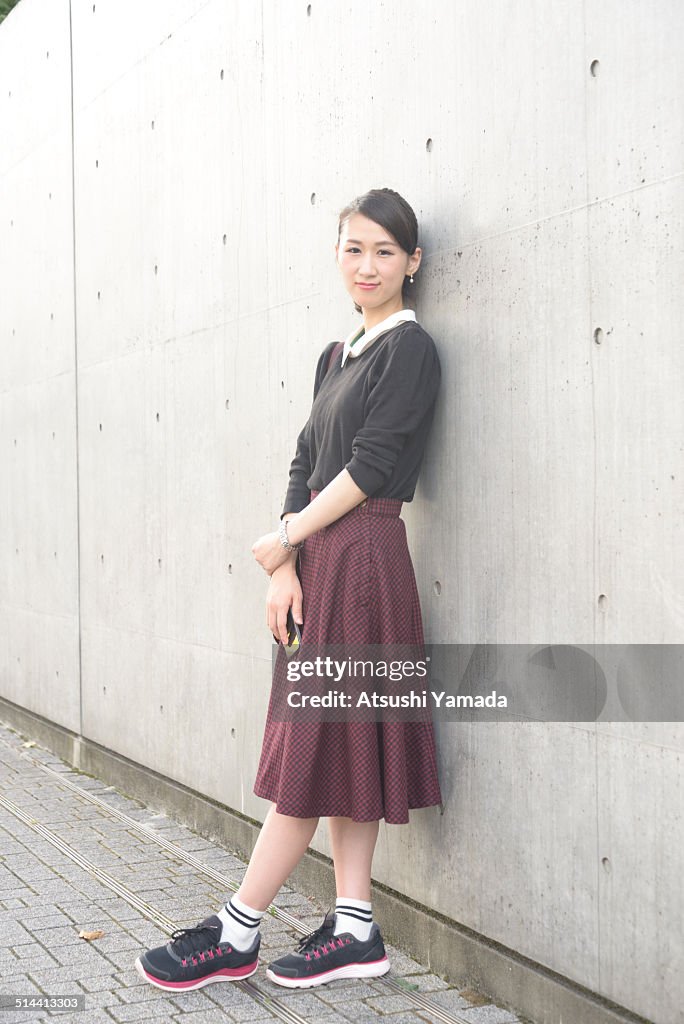 Japanese woman leaning on wall,holding cell phone