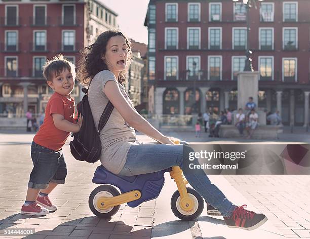 boy pushing his mother on a toy tricycle - dreirad stock-fotos und bilder