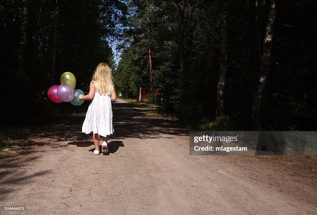 Girl (6-7) in white dress walking with balloons in her hand