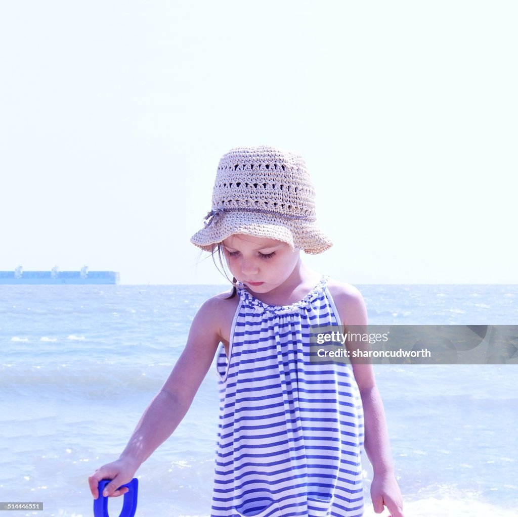 Girl in a straw hat standing on beach holding a plastic spade