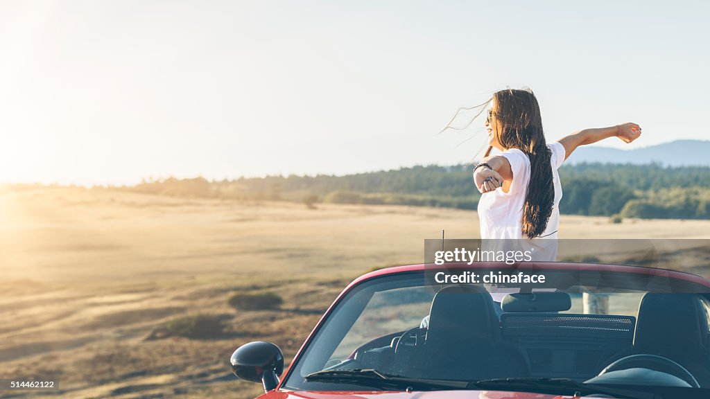 Happy asian woman standing in car with arms raised