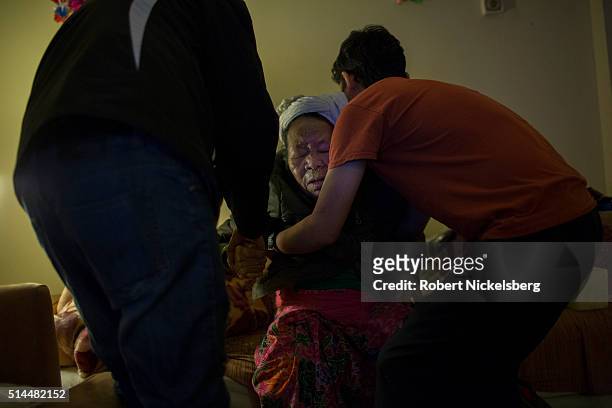 In his home, Dil Gurung helps his mother, Man Maya Gurung, into a chair, Burlington, Vermont, February 1, 2016. At left is his cousin, Santa Gurung....