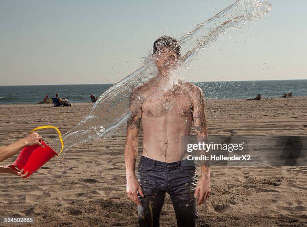 man getting splashed with bucket of water at beach - empapado fotografías e imágenes de stock